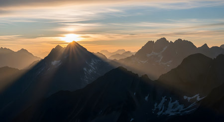 Sunlight bursts through jagged mountain peaks at dawn, casting long shadows and illuminating the sky with warm hues.の素材