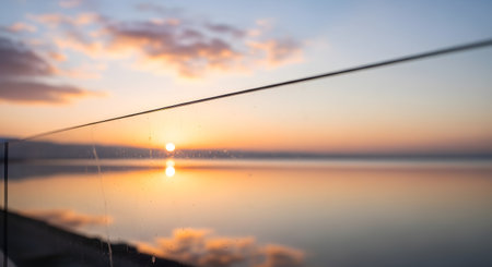 A serene sunset casts a warm golden glow across a still body of water, bisected by a thin wire.の素材