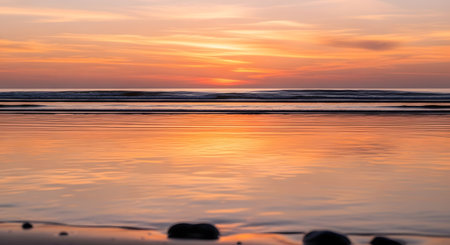 A tranquil beach scene at sunset, with the sky painted in vibrant orange and pink, reflected on the still water.の素材