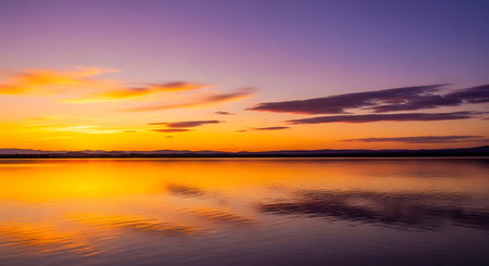 A breathtaking sunset paints the sky with fiery oranges and soft purples, mirrored perfectly on the still surface of a tranquil lake.の素材