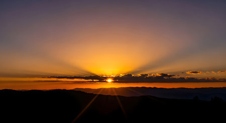 A breathtaking sunset paints the sky with vibrant orange and purple hues, as sunbeams dramatically radiate from behind dark clouds.の素材