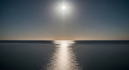 A bright sun shines down, casting a shimmering path of light across the tranquil, dark blue ocean. The horizon is a faint line.の素材