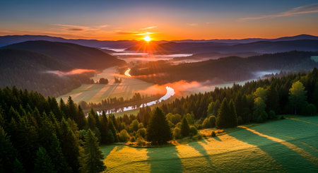 A breathtaking aerial view captures a vibrant sunrise illuminating a misty valley, a winding road, and lush green forests.の素材