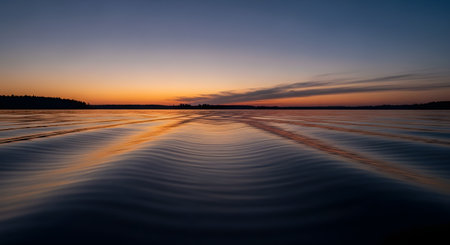 A tranquil sunset casts warm orange and purple hues across a vast body of water, creating mesmerizing ripples and reflecting the sky.の素材
