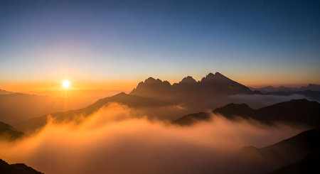 A vibrant sunrise casts a golden glow over a sea of clouds surrounding jagged mountain peaks.の素材