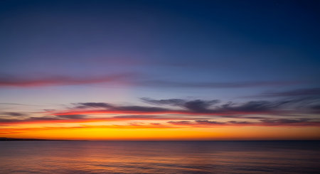 A breathtaking sunset paints the sky with fiery oranges, pinks, and purples above a tranquil ocean reflecting the colorful hues.の素材