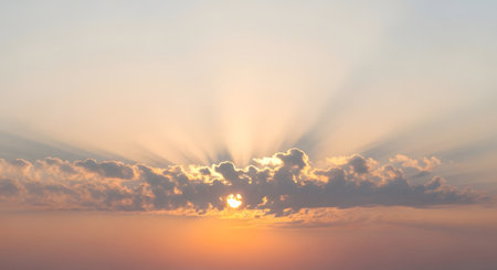 Golden sunbeams radiate from behind clouds, creating a dramatic and ethereal sky during dawn or dusk.の素材