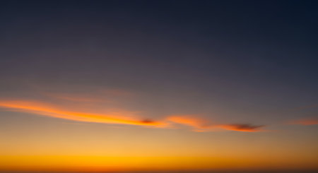 A dramatic sunset paints the sky with intense orange and yellow hues, highlighted by a single streak of fiery cloud.の素材