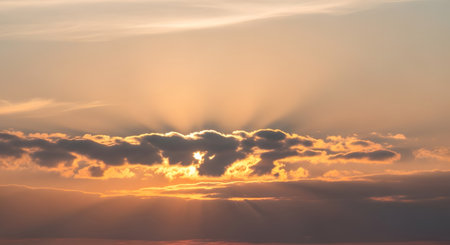 A breathtaking sunset paints the sky with warm golden hues, illuminating dramatic clouds with radiant sunbeams breaking through.の素材