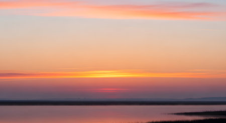 A tranquil sunset paints the sky with soft pink and orange colors, mirrored beautifully on the still water below.の素材