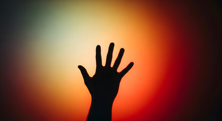 A dark silhouette of an open hand with fingers spread is cast against a vibrant, abstract background of warm, blended colors.の素材