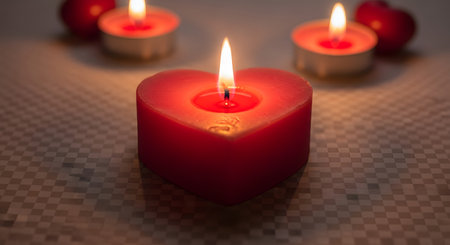 A close-up of a red heart-shaped candle with a flickering flame, surrounded by other glowing candles, creating a warm and romantic atmosphere.の素材