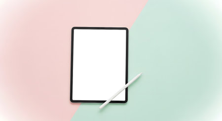 A sleek, black tablet with a blank white screen rests on a split pastel pink and mint green surface, accompanied by a white stylus.の素材
