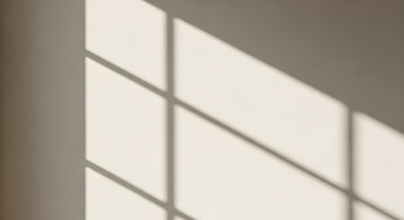 Diagonal shadows from a windowpane create a grid pattern on a plain, neutral-toned wall, suggesting a peaceful, sunlit interior.の素材