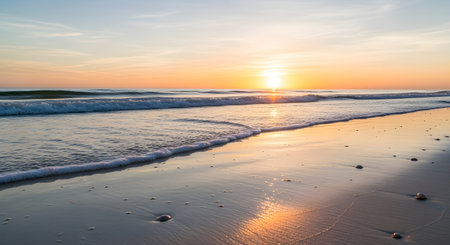 A tranquil sunrise casts a warm glow over a wet sandy beach, with gentle waves lapping at the shore.の素材