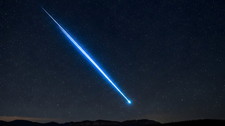 A bright blue meteor is seen streaking across a star-filled night sky, with a silhouette of mountains in the background. The meteor leaves a glowing trail as it moves through the atmosphere, creating a breathtaking scene.の素材