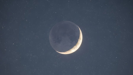 A serene image of a crescent moon shining brightly in the dark night sky, surrounded by numerous stars, capturing a moment of celestial beauty.の素材