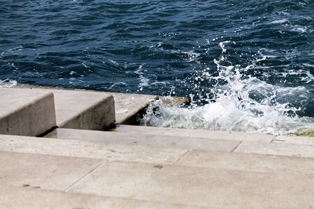 sea break wave with foam on top, on stairs of stone walkway and pierの写真素材