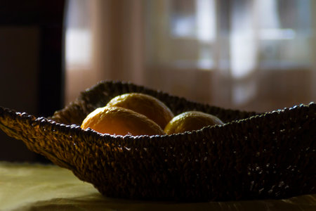 A wicker fruit basket with a few lemons on a table, a backlight in the backgroundの写真素材