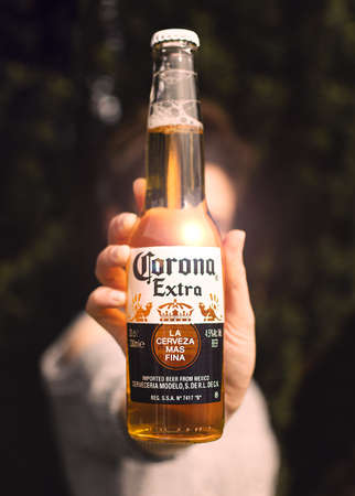 A girl holds out a bottle of Corona beer in the sunshine in a gardenのeditorial素材