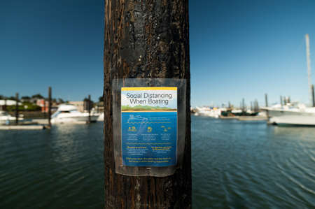 Social Distancing Guidelines sign on a pole in a harborの写真素材