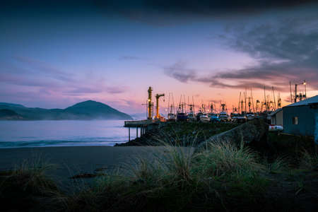Sunset over boats moored in harbor in Port Orford. Humbug Mountain in the background.の写真素材
