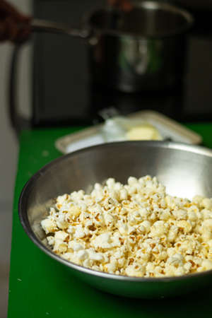 A bowl of freshly made popcorn sits on counter with butter and pot on stoveの写真素材