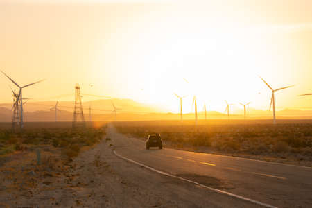 Car driving into sunset with windmills and electricity pylons
