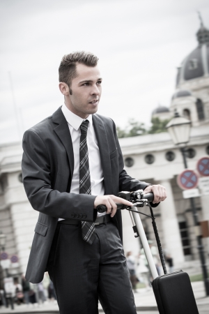 Young businessman in urban surroundings riding a pedal-scooterの写真素材