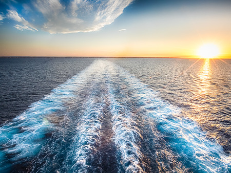 Waves and a white stream of a cruise boat in the blue ocean during the sunset.の写真素材