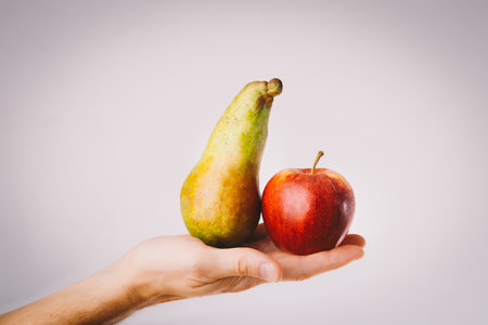 Red and green apple and pear held in male hands. Conceptual for comparison, differentiation and choice selection making.の写真素材