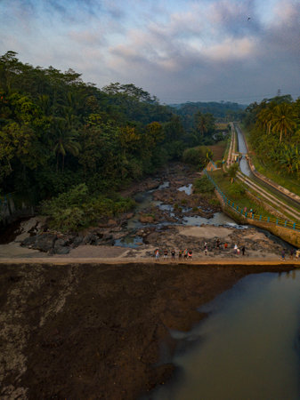 Dried dam with a small flow of water. It is surrounded by trees and looks like a rocky stream....