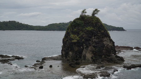 Coral rock on the beach and hit by the wave with cloudy sky.  Watu Lumbung Beach, Yogyakarta, Indonesiaの写真素材