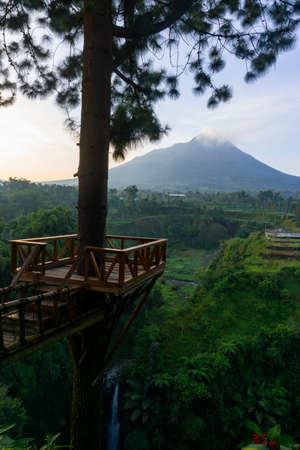 A waterfall on a cliff and surrounded by trees with Merapi Volcano on the background in the morning. Kedung Kayang waterfall, Indonesiaの写真素材