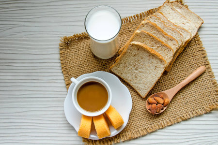 White cup of coffee with jam roll, bread, almond and milk for breakfast
