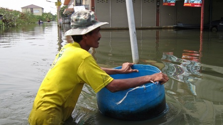 LAMLUKKA (PATHUMTHANI), THAILAND  CIRCA NOVEMBER 2011  A man with a hat pushes a barrel through the flood waters circa November 2011 in Lamlukka. The entire province has been flooded as a result of an exceptional and unprecedented rainy season. のeditorial素材