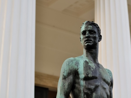 athletic male bronze statue with a longing stare in front of greek columnsの写真素材