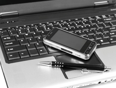 Mobile phone and pen on laptopの写真素材