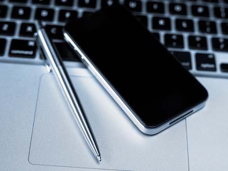 Mobile phone and pen on laptopの写真素材