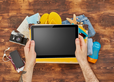Man holding a digital tablet and packing for vacationの写真素材
