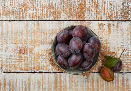 Juicy plums in a bowl on wooden tableの写真素材
