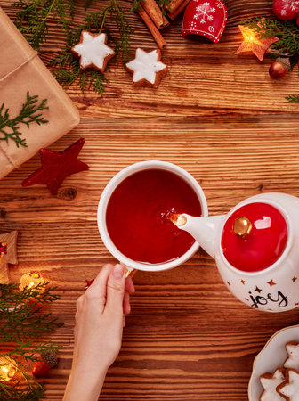 Pouring a hot cup of tea,tea cup, cookies and Christmas ornnaments on wooden tableの写真素材