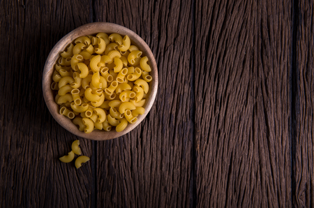 Raw pasta in wooden bowl on wood backgroundの写真素材