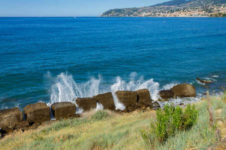 Waves against rock and, in the background, the Italian coast with the city of Sanremo