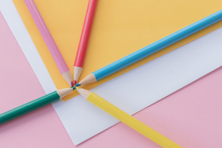Multicolored crayons on sheets of paper (yellow, white and pink)