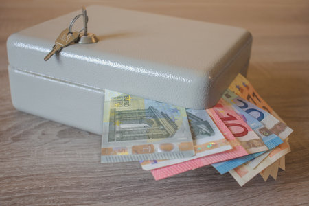 Mini vault silver safes with heaps of tickets of Euro on a wooden table