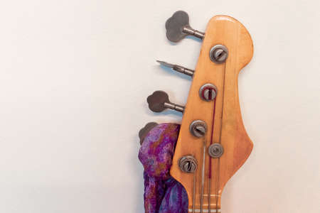 Close-up of a bass guitar with apink and violet scarf