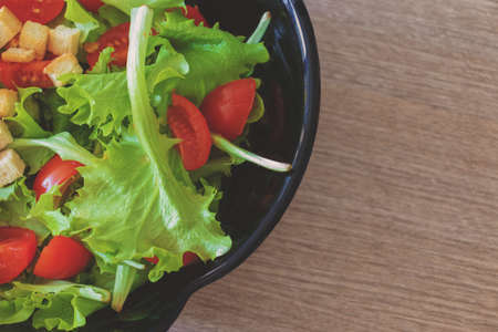 close-up of a fresh salad, tomatoes, and bread in a bowl on a wooden table. Top view. Copy spaceの写真素材