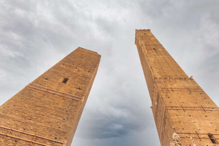 Low angle view of Asinelli (right) and Garisenda (left) towes against cloudy sky. Main medieval sights in Bologna, Italy. Copy space.の写真素材