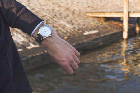 A man hand showing a time. A pier and water on the background. Concept of time, relax, lifestyle. Copy space.の写真素材